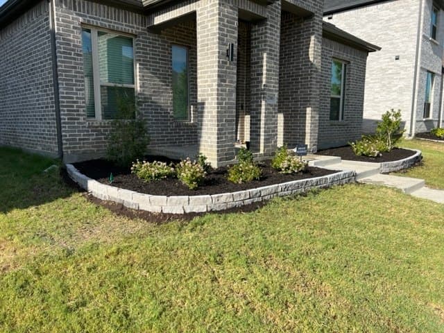 Stone-edged planting bed holding grade on a sloped Highland Village lot